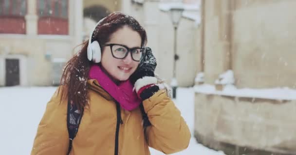 Portrait of a beautiful girl. Listening to music in the snowy city — Stock Video