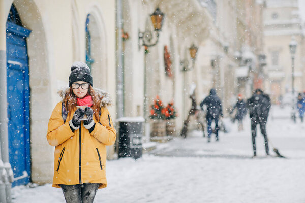 Beautiful happy woman walks around the city drinking coffee in winter city