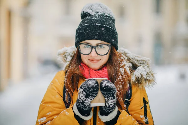 Krásná dívka chodit po městě zimní s šálkem kávy, při pohledu na fotoaparát a usmívá se — Stock fotografie