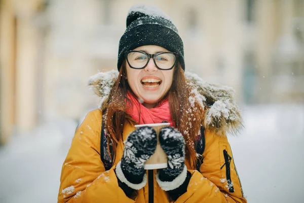 Portret van gelukkig meisje in ijzig winter stad close-up. Vliegende sneeuwvlokken. Lacht om camera, vrolijke vrolijke stemming, emoties — Stockfoto