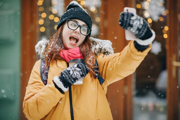 Gelukkig meisje maakt een selfie in winter stad. Meisje maakt selfie tegen de achtergrond van een winter en bevroren stad — Stockfoto