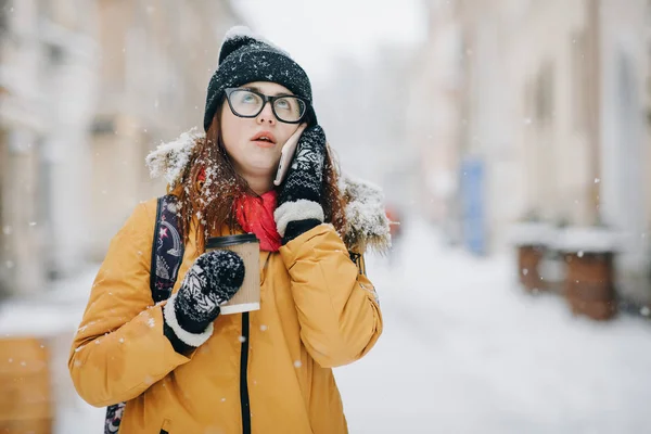 O adolescentă caucaziană vorbind la telefon râzând ţinând o ceaşcă de cafea zâmbind. În aer liber portretul de iarnă al unei adolescente frumoase vorbind la telefon — Fotografie, imagine de stoc