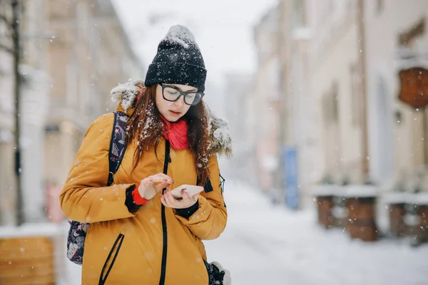 Portret van mooie gelukkig jonge vrouw met smartphone over Kerstverlichting in de winter — Stockfoto
