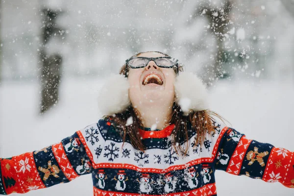 Joven mujer sonriente en chaqueta de invierno lanzando copos de nieve. Feliz hembra en hermoso bosque de pinos en la cima de la montaña rociando nieve en el aire —  Fotos de Stock
