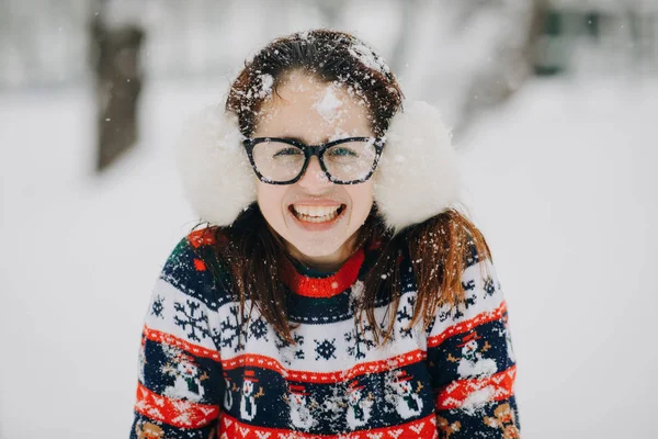 Winter portret van jong mooi meisje dragen oorwarmers, trui poseren in sneeuw park. Vrouw zoekt camera en glimlachen — Stockfoto