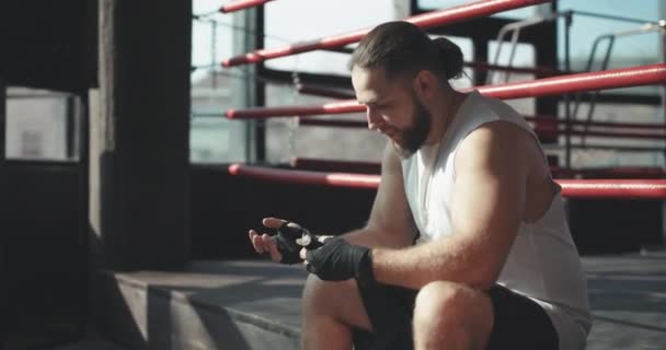 Boxer legt Handschellen an, während er am Rande eines Boxrings in einer Boxsporthalle sitzt, Kamera dreht sich — Stockvideo