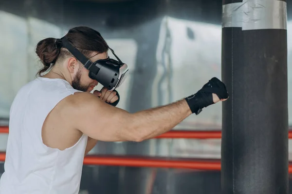 Young man boxer in VR 360 headset training for kicking in virtual reality combat