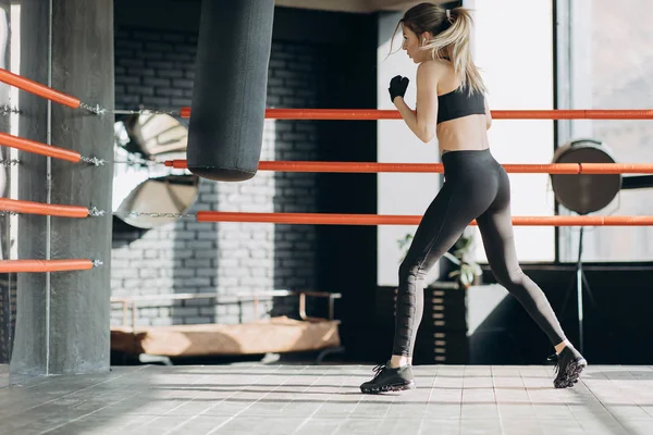 Mujer Kickboxing en airpods saco de boxeo de entrenamiento en estudio de fitness cuerpo en forma de fuerza feroz — Foto de Stock