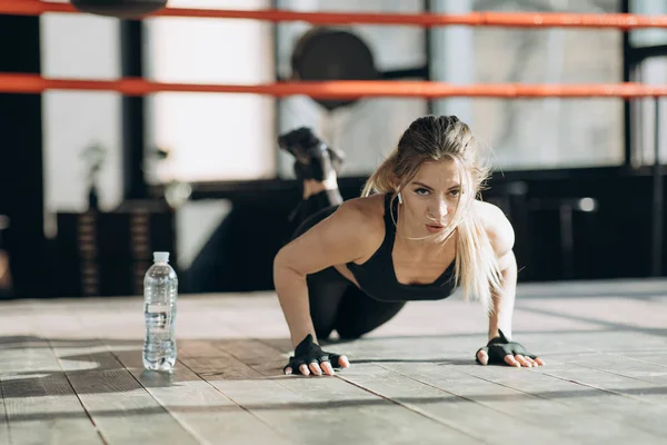 Mujer bonita mirando a la cámara mientras hace flexiones desde el suelo de madera en el gimnasio — Foto de Stock