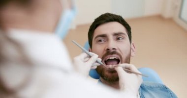 Neşeli yakışıklı adam kamera bir diş hekimi onun dişçi arka planda diş kontrolü için hazırlanıyor oturan gülümseyen