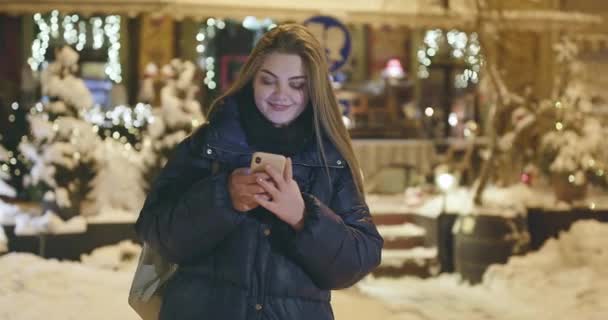 Mujer usando teléfono móvil durante un paseo por las calles de la ciudad nocturna — Vídeo de stock