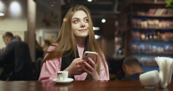 Mujer escribiendo mensaje de texto en el teléfono inteligente en un café con un café — Vídeos de Stock