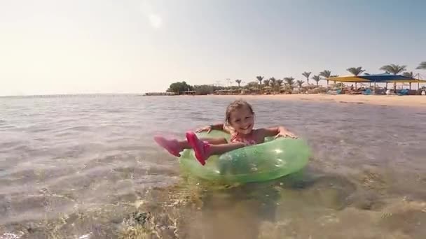 Petite fille jouant avec l'anneau gonflable coloré dans la piscine extérieure le jour chaud d'été. Les enfants apprennent à nager. Vacances familiales à la plage — Video