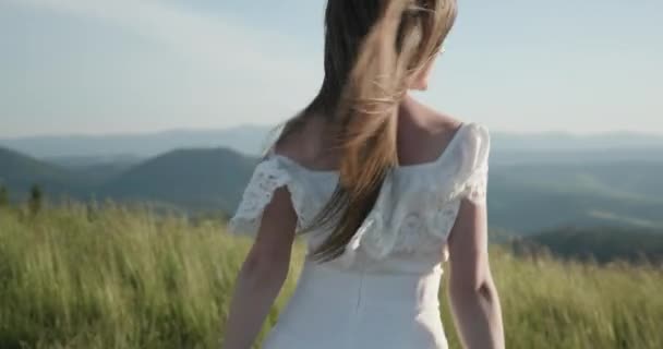 Aantrekkelijke vrouw op een bergtop met haar lange haren waait in de wind glimlachend en probeert haar haar van haar gezicht te houden — Stockvideo