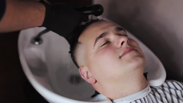 Barbershop. Een jonge kerel krijgt een kapsel en haarverzorging service van een bebaarde man met een haar vastgebonden op zijn hoofd. — Stockvideo