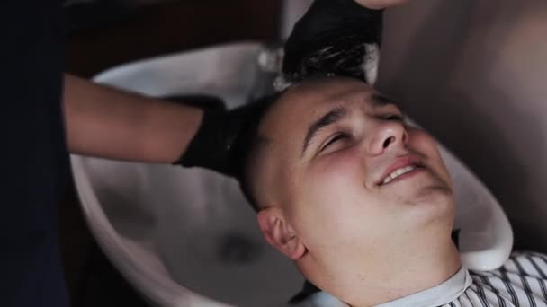 Νέος άντρας να πλένει τα μαλλιά του από έναν αγνώριστο κουρέα σε ένα κουρείο. — Αρχείο Βίντεο