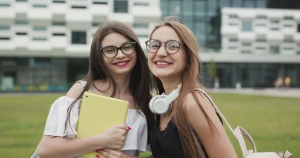 Две счастливые кавказские девушки лучшие друзья веселятся в модных солнцезащитных очках, позируют на открытом воздухе, смотрят в камеру — стоковое видео