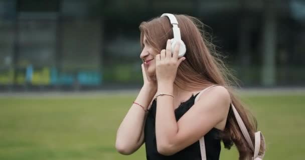 Joven chica atractiva en el fondo urbano escuchando música con auriculares 4k — Vídeo de stock