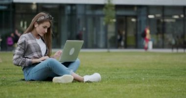 Kız internet te bilgi aramak için bir dizüstü bilgisayar kullanarak. Güzel bir kadın üniversite öğrencisi kamu bahçe yakınında çim gölgesinde oturur.