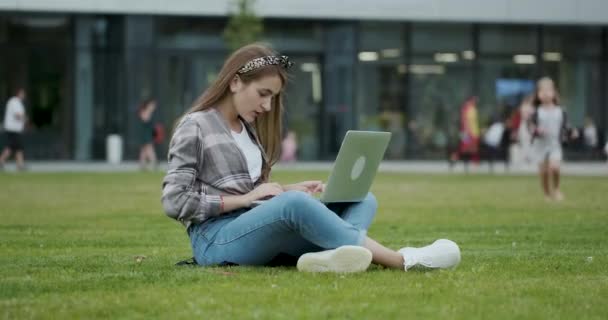 Νεαρό κορίτσι φοιτητής χρησιμοποιώντας φορητό υπολογιστή, ενώ κάθονται σε ανοιχτό αέρα. Κορίτσι χρησιμοποιώντας ένα φορητό υπολογιστή για να δείτε πληροφορίες στο διαδίκτυο — Αρχείο Βίντεο