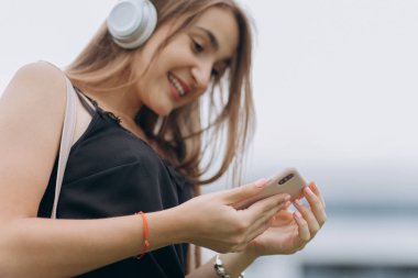 Akıllı telefon kullanan, mesaj yazan, müzik dinleyen, şehir caddesinde yürüyen genç bir kadın. Yakın çekim