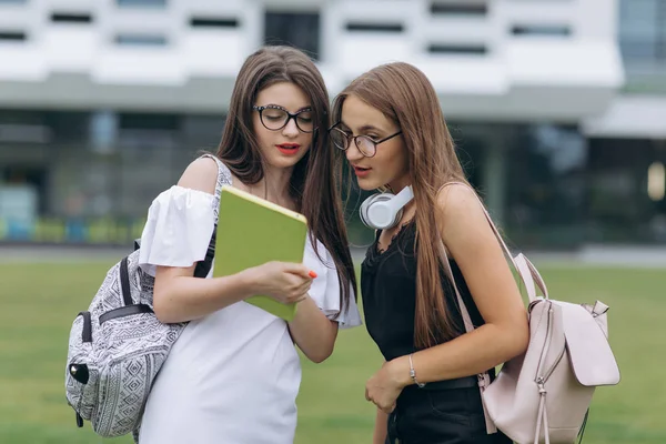 Casual styl studentów chodzić wzdłuż Uniwersytetu nowoczesnego budynku, mają przyjemną rozmowę. Dwie nastoletnie dziewczyny rozmawiają razem w kampusie. Dwie studentki college'u stojąc na zewnątrz duży budynek miejski — Zdjęcie stockowe