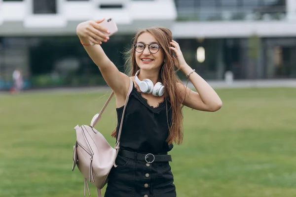 Joyeux souriant jeune écolière dame aux cheveux longs portant des lunettes regardant caméra prendre un selfie . — Photo