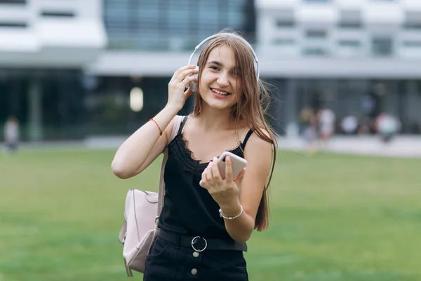Atrakcyjna młoda kobieta słuchając muzyki w smartfonie używać smartphone na spacer po zachodzie słońca i uśmiech — Zdjęcie stockowe