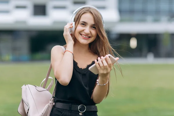 Ελκυστικό νεαρό κορίτσι σε δρόμους της πόλης στο παρασκήνιο ακούγοντας μουσική με ακουστικά — Φωτογραφία Αρχείου