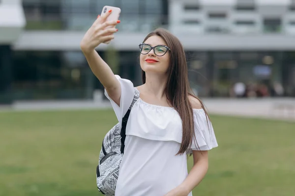 Szép, fiatal, boldog, izgatott üzleti nő a gyaloglás a szabadban közel üzleti központ viselése szemüvegek vesz selfie által kamera — Stock Fotó