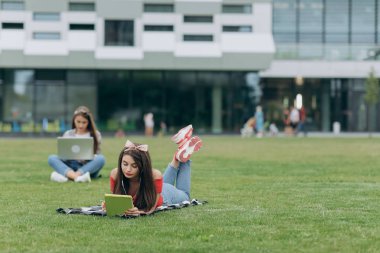 Serbest çalışmaya çalış. Öğrenci öğrenimi. Yeşil çimenlerin üzerinde oturan iki güzel kız arkadaş.