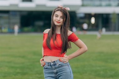 Haki üst ve yırtık kot uzun seksi sağlıklı saçları ile güzel esmer kadın. Kadın üniversite öğrencisi kameraya bakarak mutlu gülümseyerek.