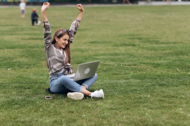 Yeşil çimenlerin üzerinde dizüstü bilgisayarla parkta oturan kadın. Açık havada eğitim alan öğrenci