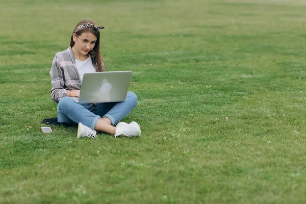 Woman sitting on green grass in park during summer day while using laptop — Stock Photo, Image