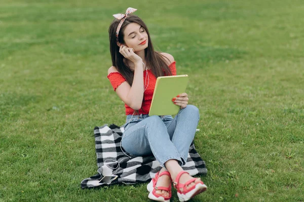 Žena naslouchající hudbě přes sluchátka a čtení knih v parku — Stock fotografie