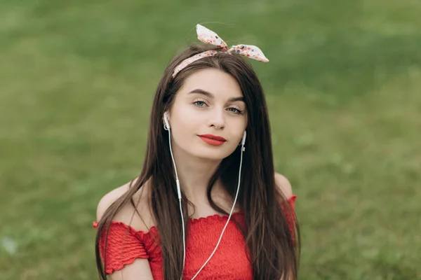 Müzik dinleyen kadın. Parkta yeşil çimenlerin üzerinde oturan ve müzik dinleyen genç kadın — Stok fotoğraf