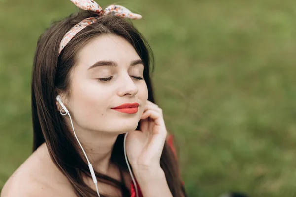 Vrouw die naar de muziek luistert. Portret van aantrekkelijke jonge vrouw zittend op groen gras in Park en luisteren naar de muziek — Stockfoto