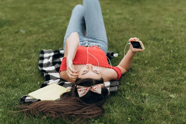 Kobieta słucha muzyki. Dziewczyna odpoczywa na trawie i słucha muzyki — Zdjęcie stockowe