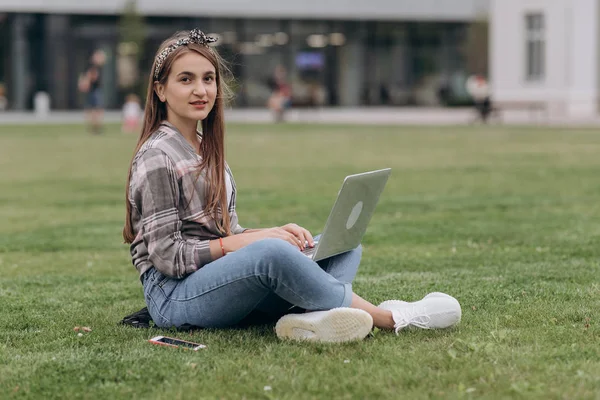 Woman sitting on green grass in park during summer day while using laptop — Stock Photo, Image