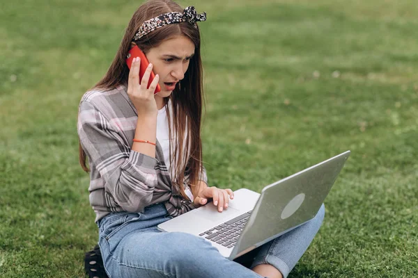 Woman working with laptop and smartphone while sitting in garden with green grass. Concept of people using mobile technology. — Stock Photo, Image