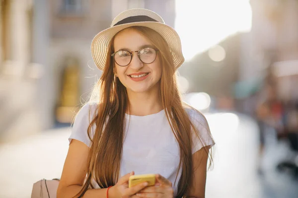 Fille marchant dans la rue et SMS SMS sur son téléphone mobile. Attrayant jeune femme dans un look élégant en utilisant APP sur son iPhone. Réseaux sociaux. Être en ligne . — Photo