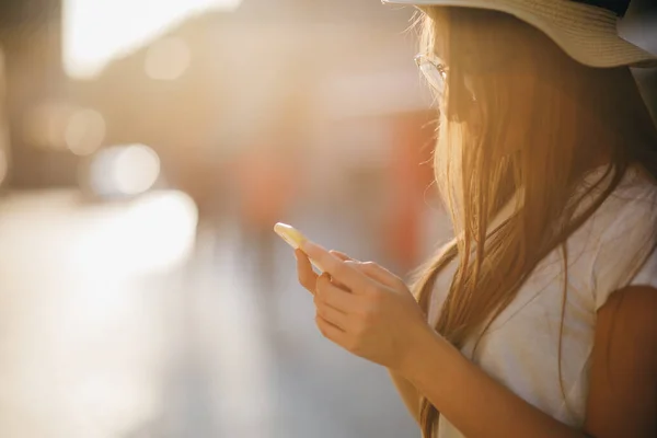 Femme voyageuse bouclée dans un chapeau et des lunettes avec un téléphone dans ses mains, sur un fond de printemps lumineux au soleil — Photo