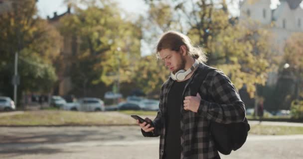 Człowiek korzystający z aplikacji na smartfonie spacerując po mieście. Przystojny młody człowiek komunikuje się na smartfonie pewny siebie. Miejski mężczyzna dojeżdżający do pracy w wieku 20 lat — Wideo stockowe