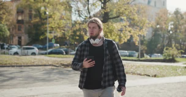 Drinkwater uit sport shaker na fitness training na het sporten, Outdoor sport brunette man drinken helder mineraalwater na de training en het gebruik van de smartphone in de straat. — Stockvideo