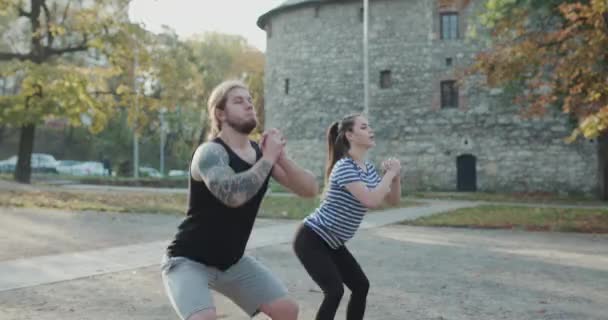 Een paar oefeningen in het park. Training voor perfecte heupen. Atletische jonge vrouwen en mannen in sportkleding doen fysieke oefeningen met coach in groen park buiten. — Stockvideo