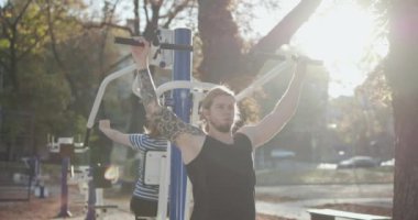Gün batımında spor salonunda mükemmel vücutlu kaslı bir atletik. Kollarını çalıştıran güçlü, formda bir adam. Parktaki spor salonunda çift eğitimi, sağlıklı yaşam tarzı, gri saç, birlikte zaman geçirmek.