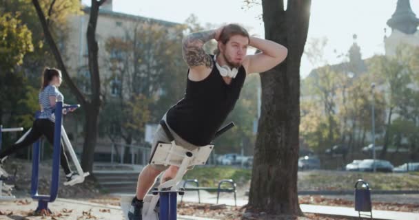 Atletické mladé ženy a muž ve sportovním oblečení dělat fyzická cvičení s trenérem v zeleném parku venku. Trénink na dokonalé boky. Pár cvičení v parku. — Stock video