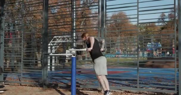 Attractive sportsman training forearms, biceps and triceps at the outdoor gym. Guy trains in city park. Handsome young man doing outdoors workout for arms. — Stock Video