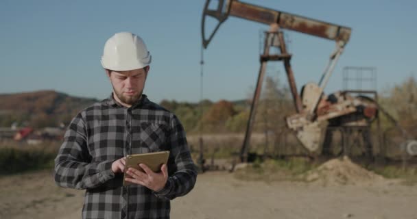 Engineer, blurred background holding digital tablet and looking at camera. Developer of the European appearance looks through the camera and makes a sketch in the tablet. — Stockvideo