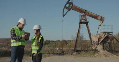 Petrol pompalama ünitesinin yanında çalışan mühendisler. Hard Hats 'taki Erkek ve Kadın Endüstriyel Mühendisler Tablet Bilgisayar Kullanırken Yeni Projeyi Tartışıyor.